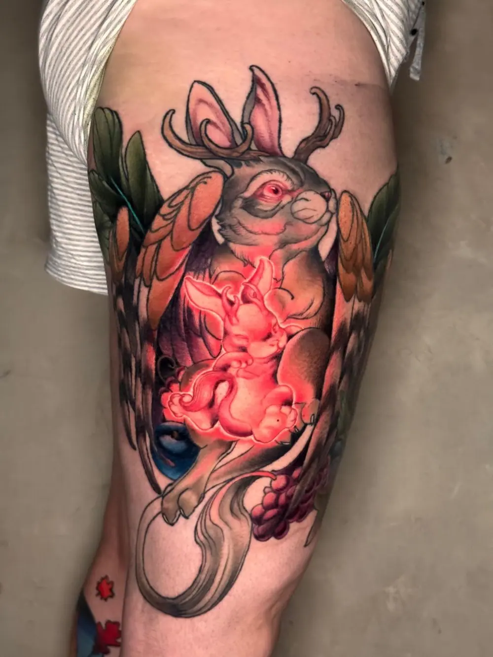 Thigh tattoo: a jackalope, a horned hare, holding a glowing red and white bunny