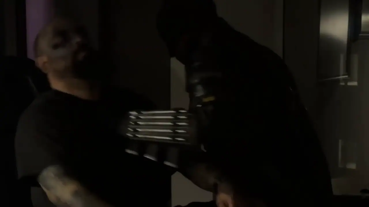 Scene from the video: the vigilante in the black suit facing a client at the studio